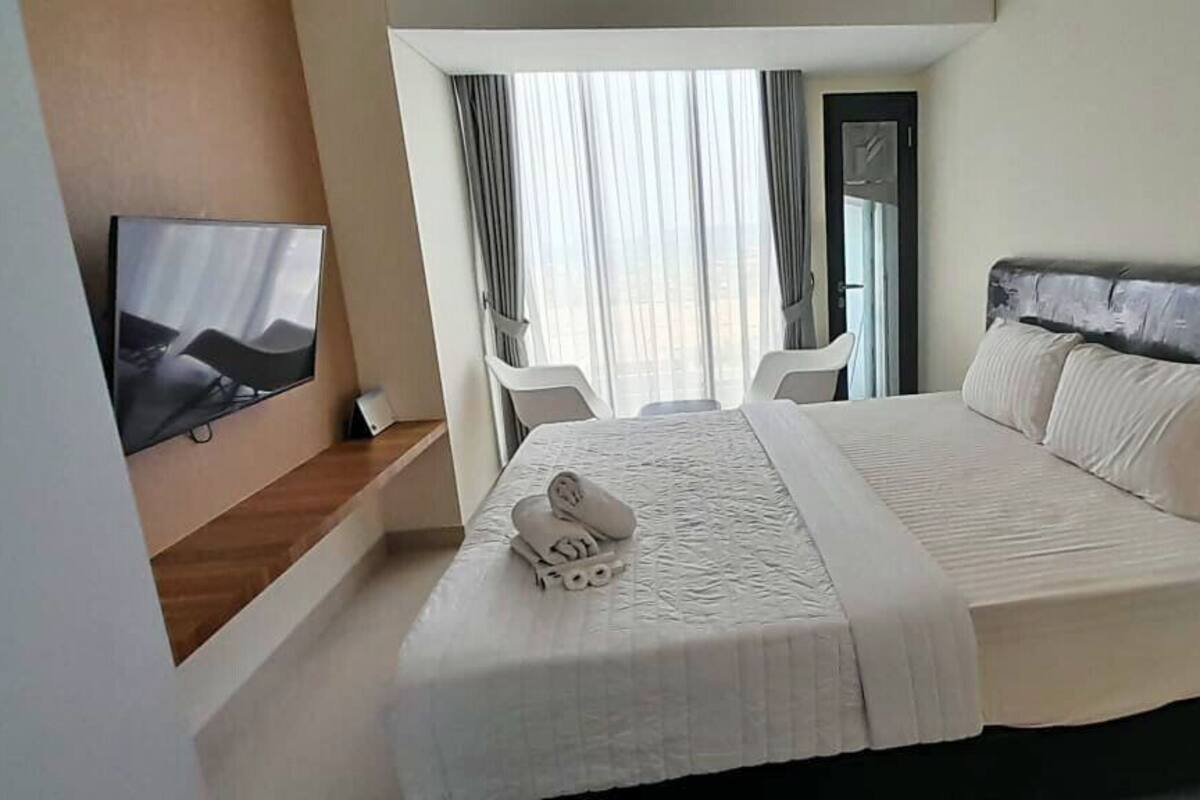 Ein Hotelzimmer mit einem großen Bett, einem flachbildfernseher an der Wand und einem Fenster mit Vorhängen.