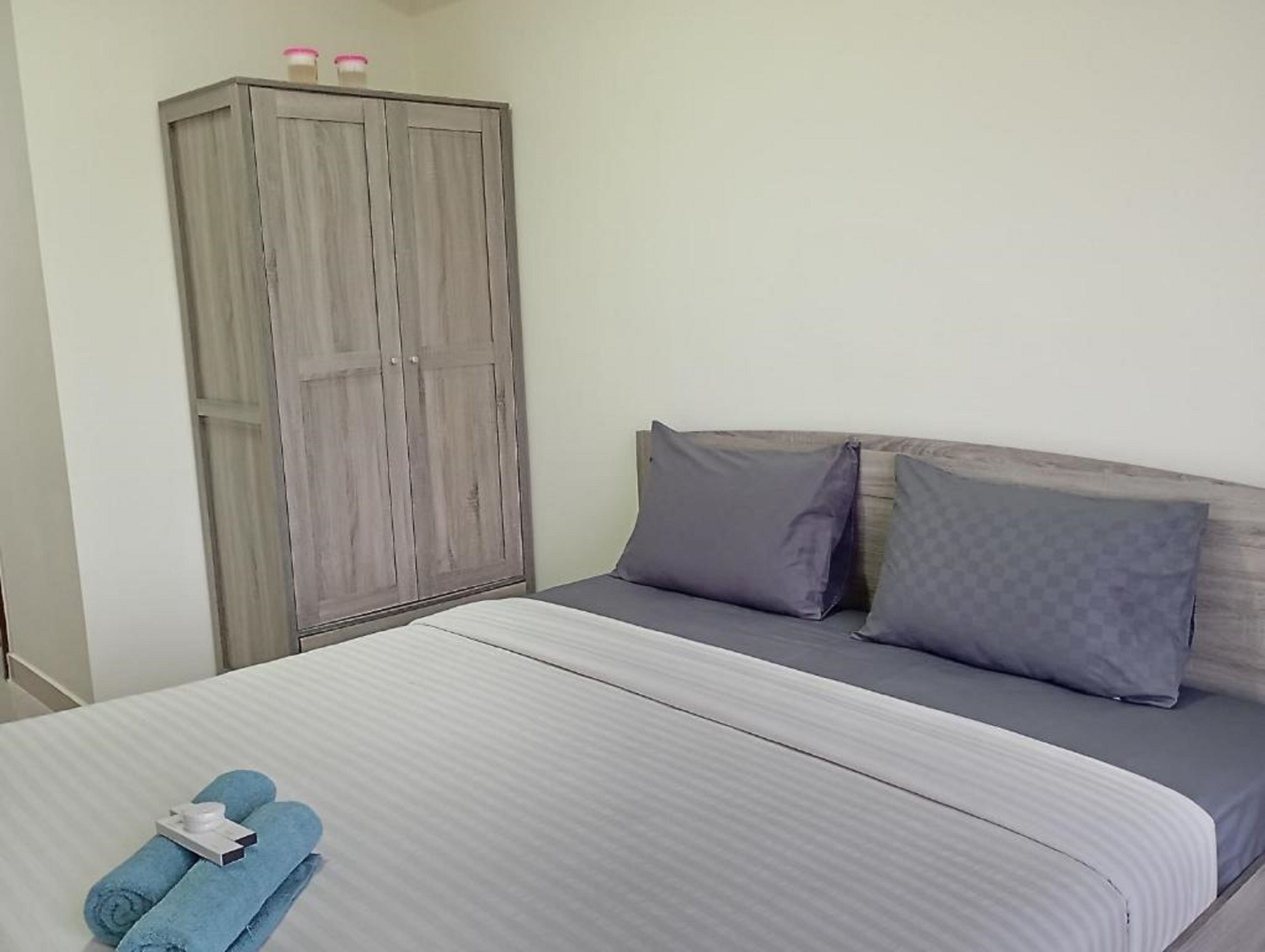 A bedroom with a bed, grey pillows, a wardrobe, and two bottles on top.