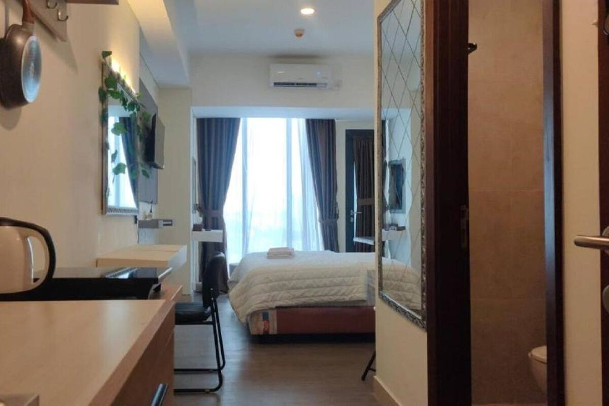 Ein Hotelzimmer mit Bett, Schreibtisch mit Wasserkocher, Spiegel und Fenster mit Vorhängen.