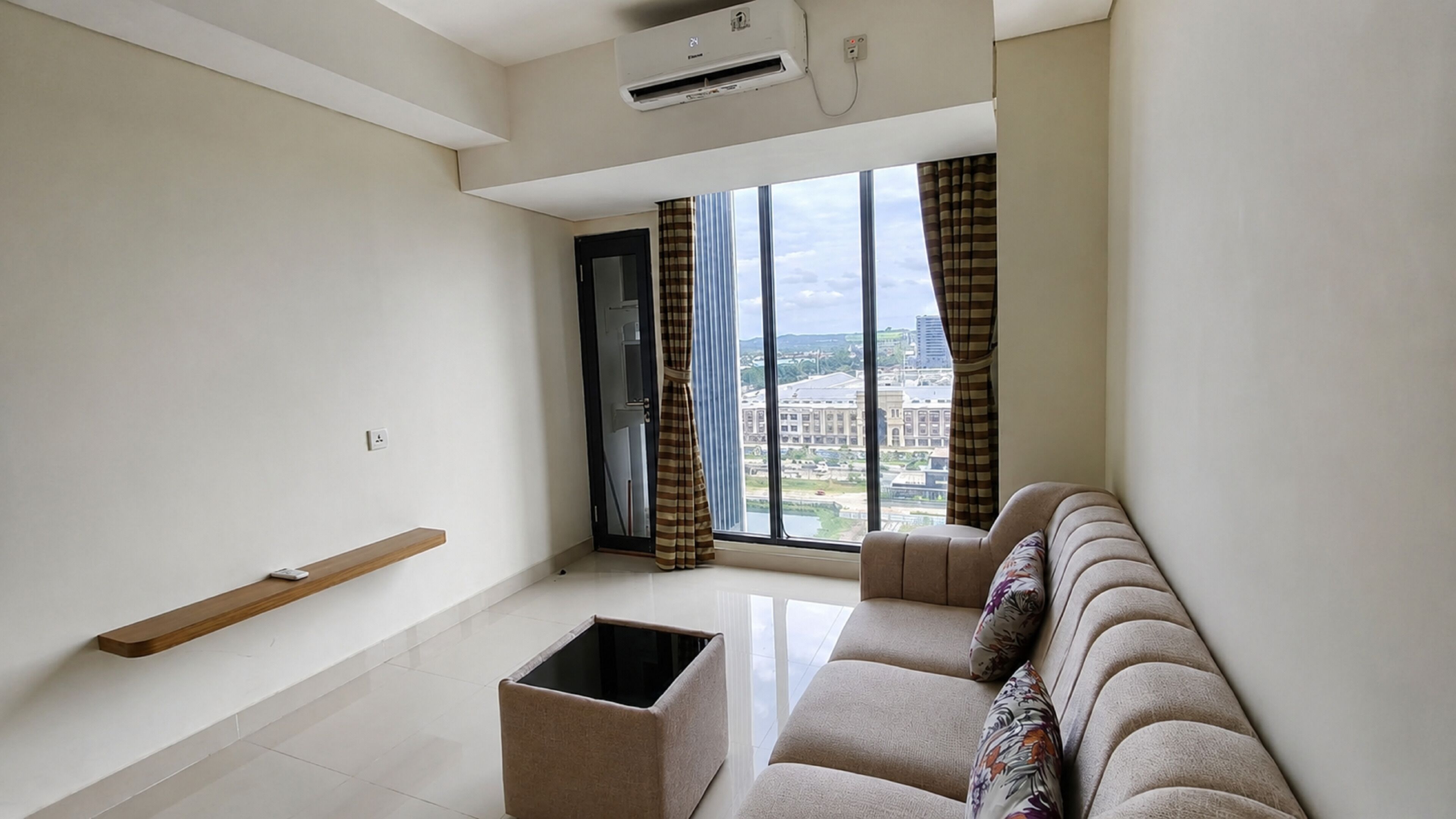 A modern living room with a sofa, a small table, and a window with a city view.