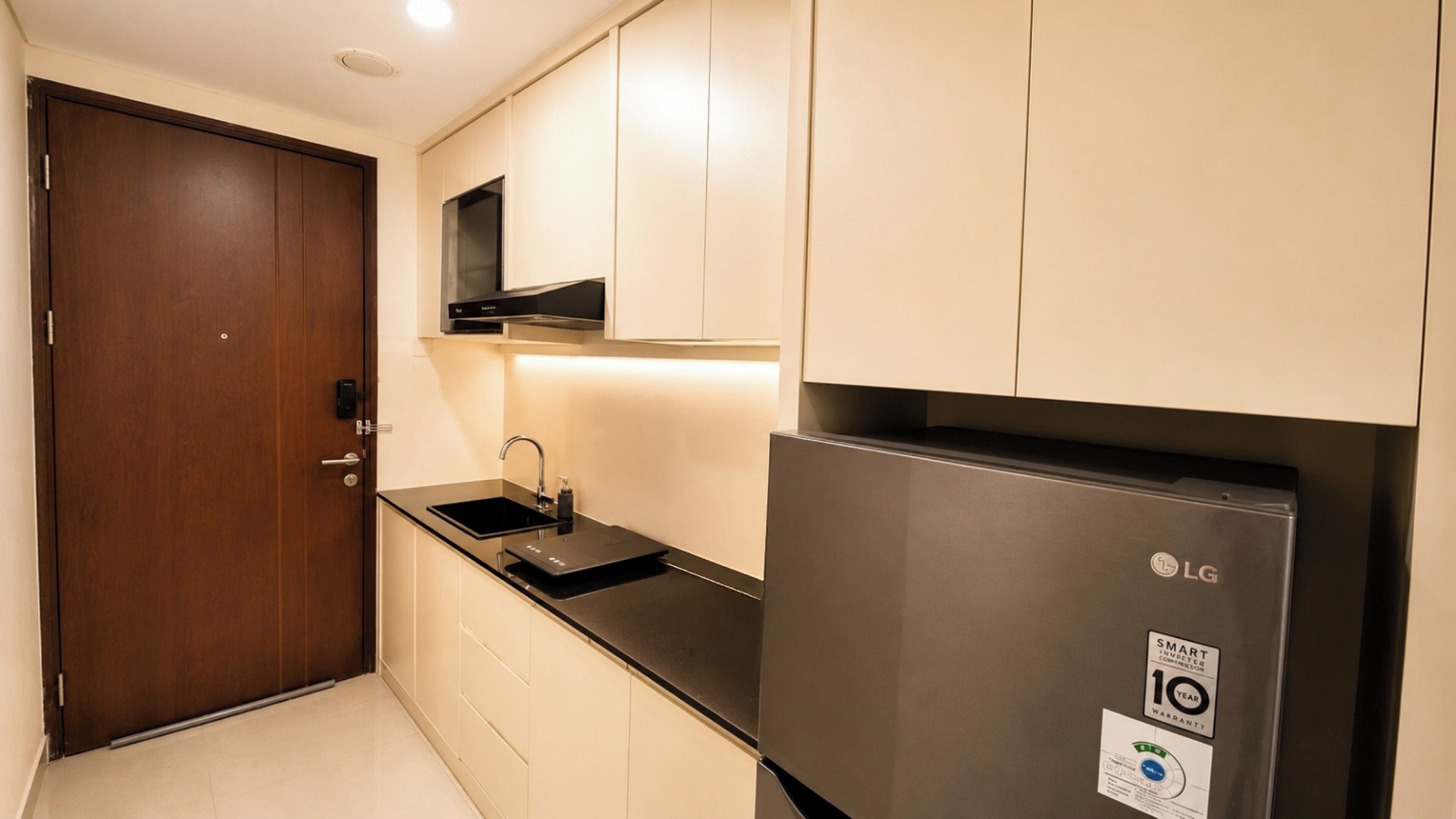 A compact kitchen with a stainless steel refrigerator, a microwave, and a sink.