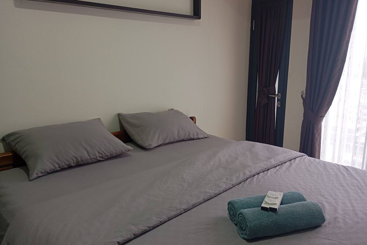 Ein ordentlich bezogenes Bett mit grauer Bettwäsche, einem Holz-Kopfteil und einem Paar türkisfarbener Handtücher.
