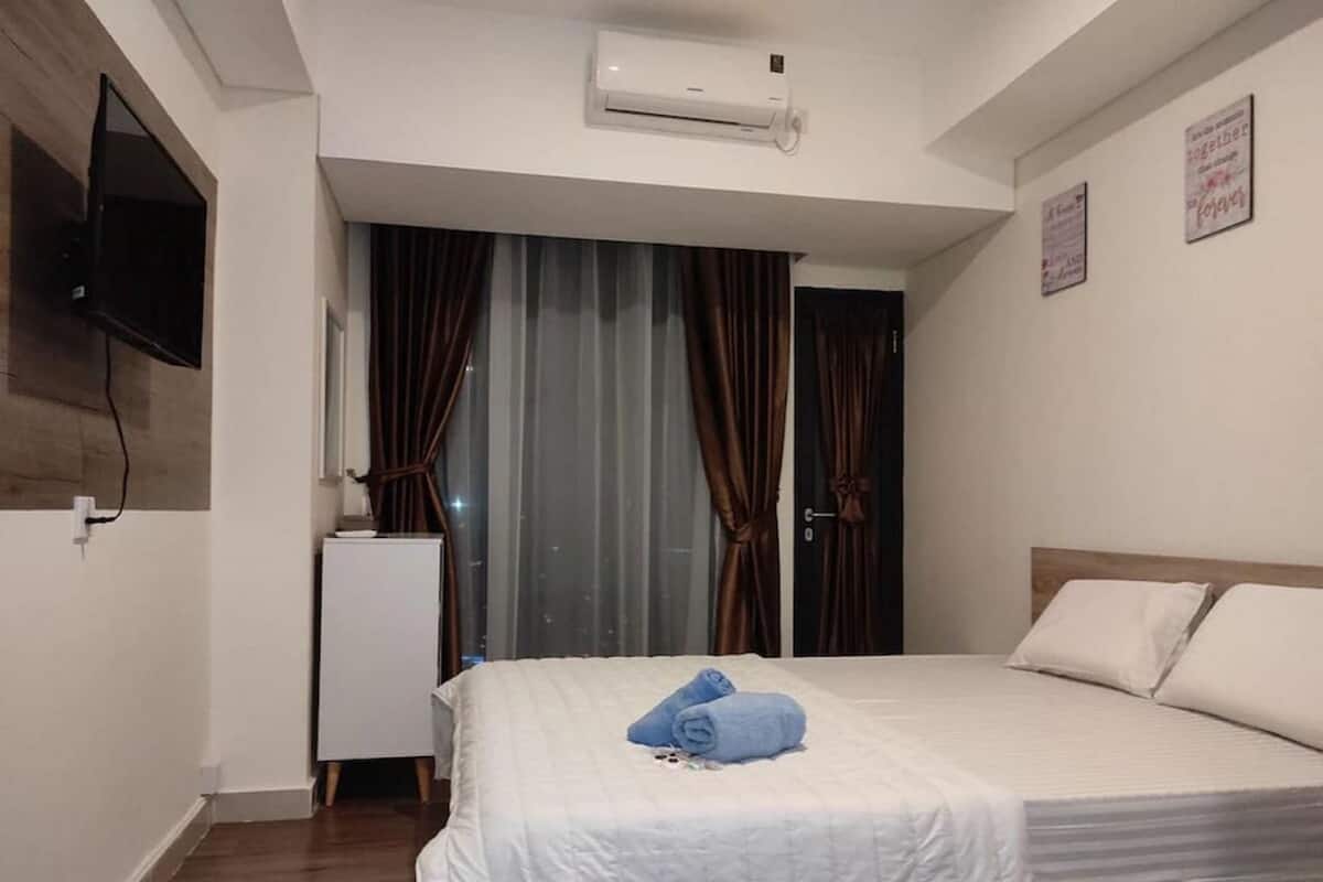 Ein Hotelzimmer mit Bett, Wandfernseher, Klimaanlage und kleinem Kühlschrank.