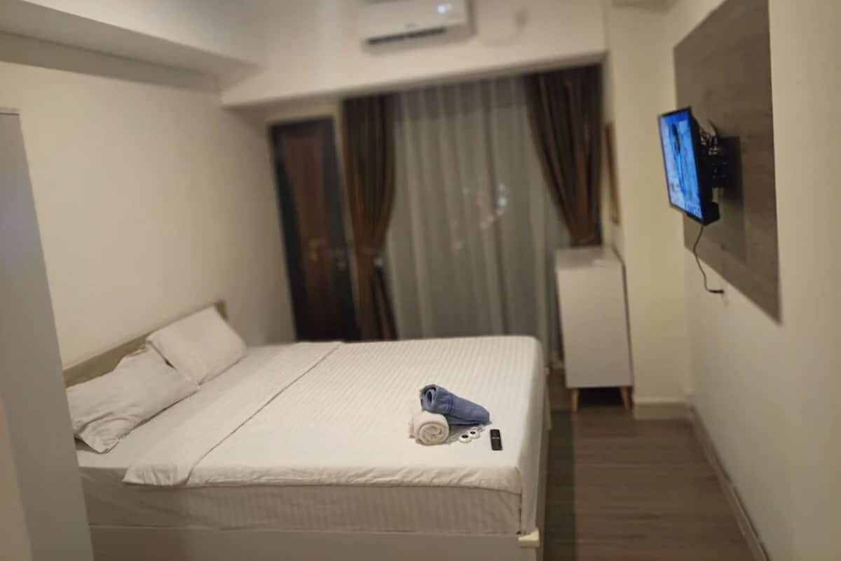 Ein Hotelzimmer mit Bett, Wandfernseher und einem Vorhangfenster.