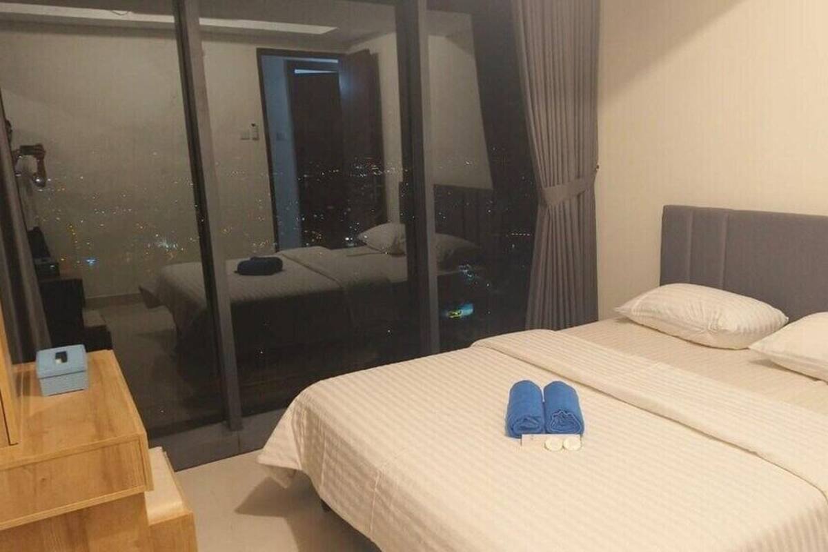 Ein Hotelzimmer mit einem Bett, einem Nachttisch aus Holz, einer Glastür, die auf einen Balkon mit Blick auf die Stadt führt, und einem Vorhang.