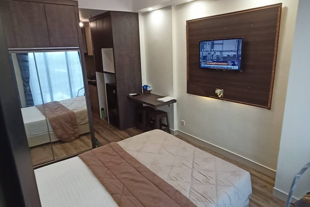 Ein Hotelzimmer mit einem Bett, einem Schreibtisch, einem an der Wand befestigten Fernseher und einem Fenster mit Vorhängen.