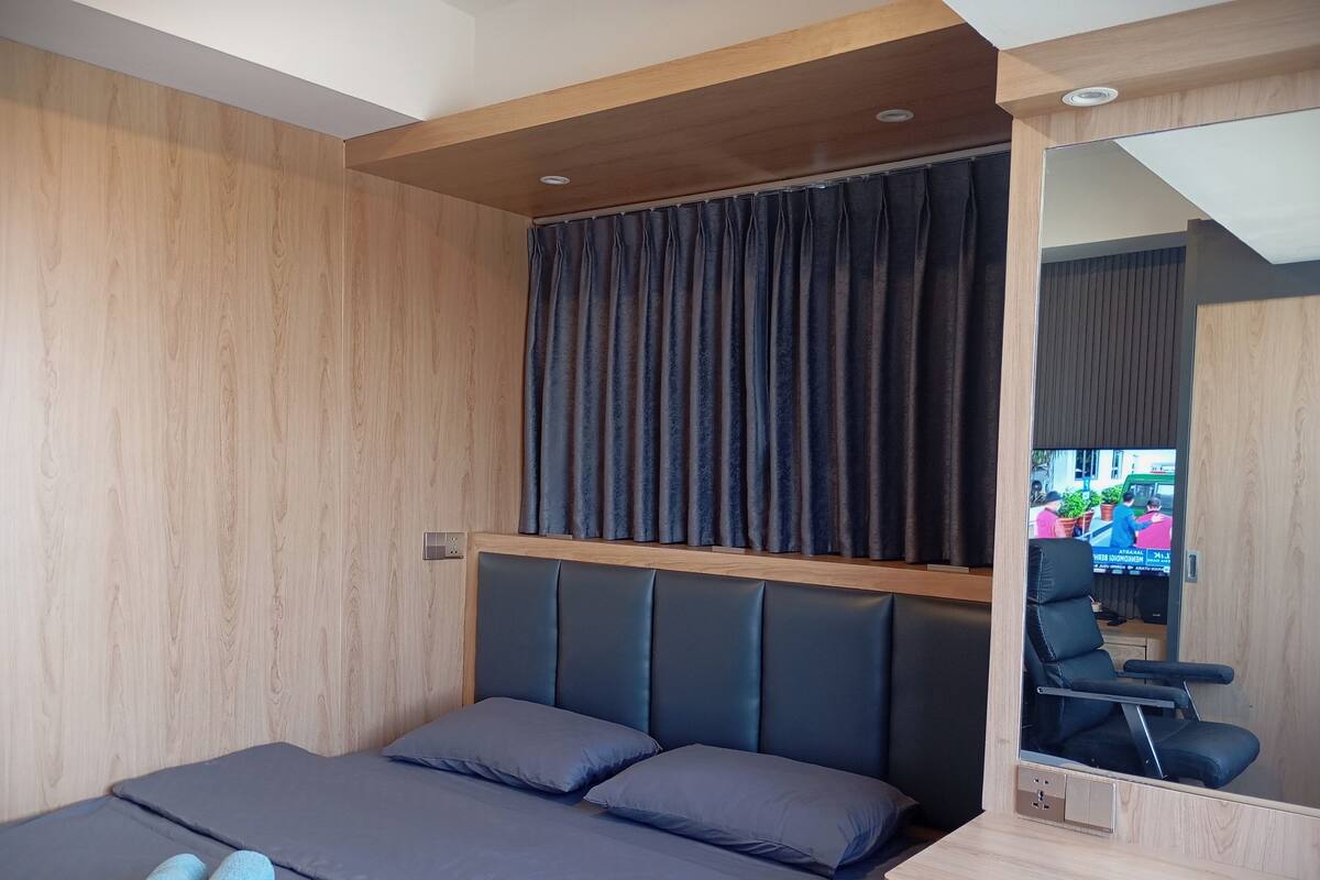 Ein modernes Hotelzimmer mit einer Wandpaneele aus Holz, einem großen Bett mit grauer Bettwäsche, einem Kopfteil und einem Spiegel an der Wand.