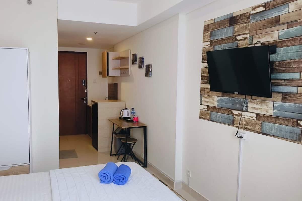 Ein Hotelzimmer mit einem Bett, einem Schreibtisch, einem Stuhl, einem Kleiderschrank und einem an einer Wand mit rustikaler Holzpaneelausstattung montierten Fernseher.