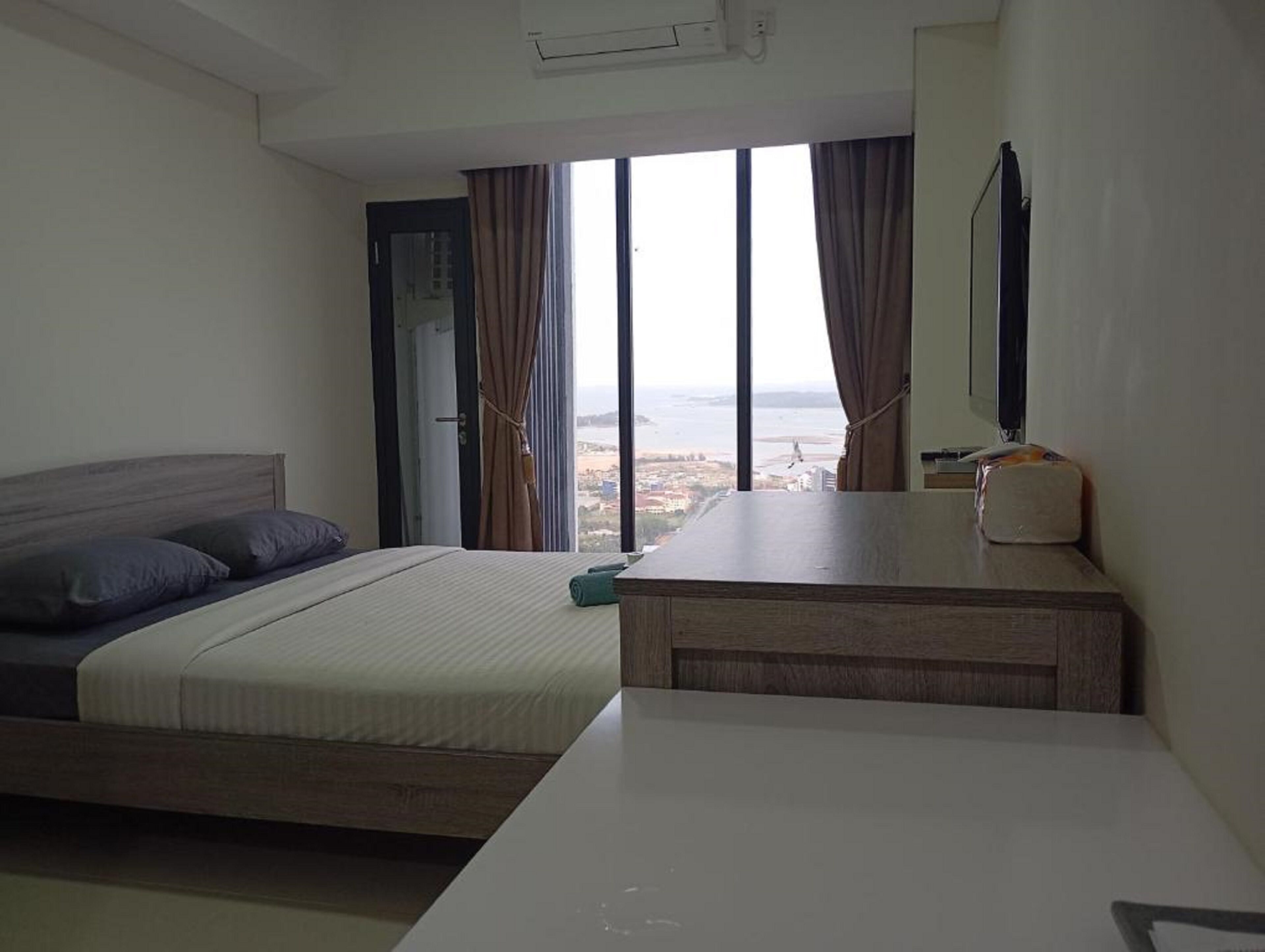 Habitación de hotel con cama, mesita de noche, televisor y vistas a la ciudad y al mar.