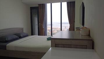 Habitación de hotel con cama, mesita de noche, televisor y vistas a la ciudad y al mar.