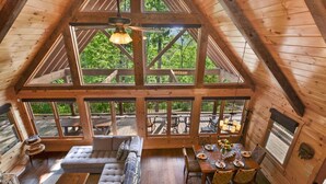 A spacious wooden cabin with a high ceiling, large windows, a dining area, and a cozy seating area.
