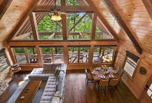 Una cabaña de madera espaciosa con techo alto, ventanas grandes, comedor y zona de estar acogedora.