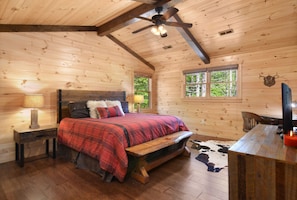 Un dormitorio de cabaña de madera acogedor, con una cama, un banco, un escritorio y un ventilador de techo.