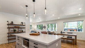 A spacious kitchen with a large island, wooden shelves, and pendant lighting. - The Lake Hut - a perfect place to relax and play on shore of Lake Whatcom (Sedro Woolley)
