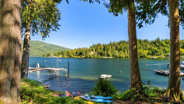 A serene lakeside view with docked boats, a sailboat, and kayaks. - The Lake Hut - a perfect place to relax and play on shore of Lake Whatcom (Sedro Woolley)