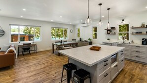 A modern kitchen with a large island, wooden flooring, and pendant lighting. - The Lake Hut - a perfect place to relax and play on shore of Lake Whatcom (Sedro Woolley)