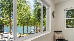 A room with a large window overlooking a lake, a chair, and a clock on the wall. - The Lake Hut - a perfect place to relax and play on shore of Lake Whatcom (Sedro Woolley)