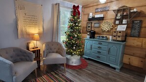 A cozy living room with two armchairs, a Christmas tree, a coffee station, and a wall with a poem.