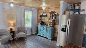 A cozy kitchen with a brick wall, two armchairs, a teal dresser, and a refrigerator.