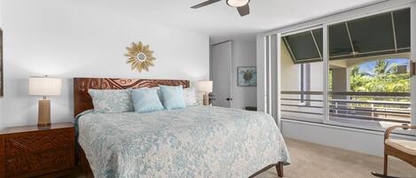A bedroom with a bed, nightstands, a ceiling fan, a window with a view, and a decorative wall piece.