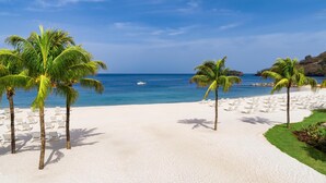 Une plage de sable blanc, des palmiers et un bateau sur l’eau.