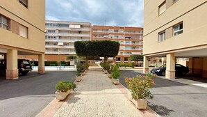 A courtyard with a central pathway lined with potted plants, surrounded by multi-story buildings with balconies and parking spaces. - 080 - Gaviotas 004 - comfortHOLIDAYS (Santa Pola)