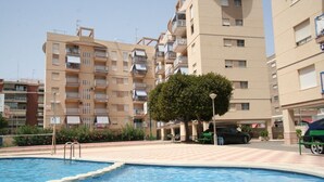 A swimming pool with steps leading into it, surrounded by a paved area with a tree and a parked car. - 080 - Gaviotas 004 - comfortHOLIDAYS (Santa Pola)