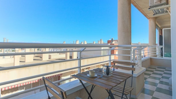 Een balkon met een zwart-wit geruite vloer, een houten tafel met een kopje en schotel, en een vaas.