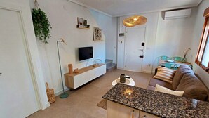 A modern living room with a TV, a dining area with a table and chairs, and a kitchen area with a granite countertop. - 082 - Gran Playa 005 - comfortHOLIDAYS (Santa Pola)