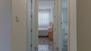 A narrow hallway leading to a bedroom with a bed, a nightstand, and a lamp. - 084 - Isabel La Católica - comfortHOLIDAYS (Santa Pola)