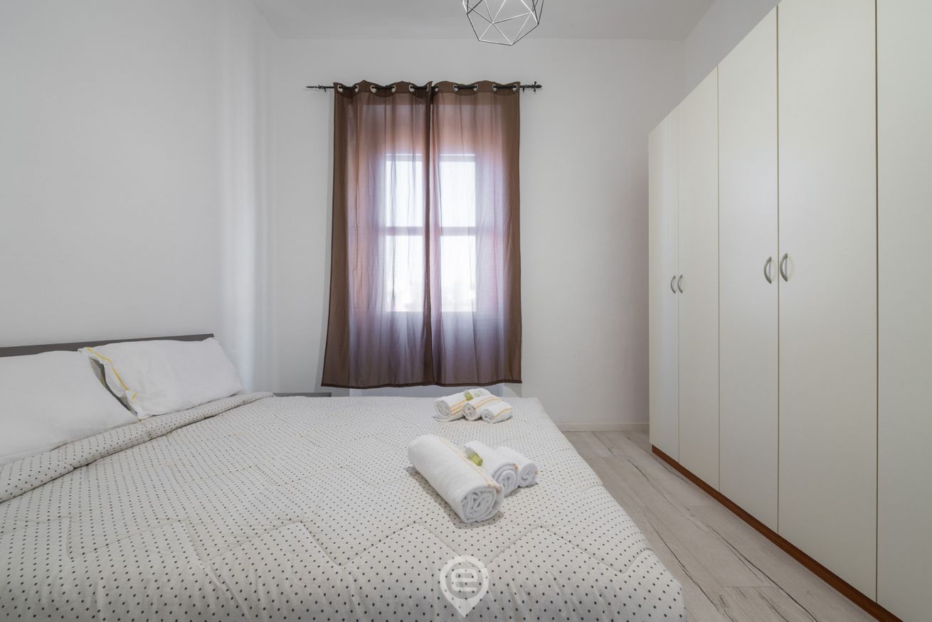 Ein Schlafzimmer mit Bett, Kleiderschrank und einem Fenster mit Vorhängen.