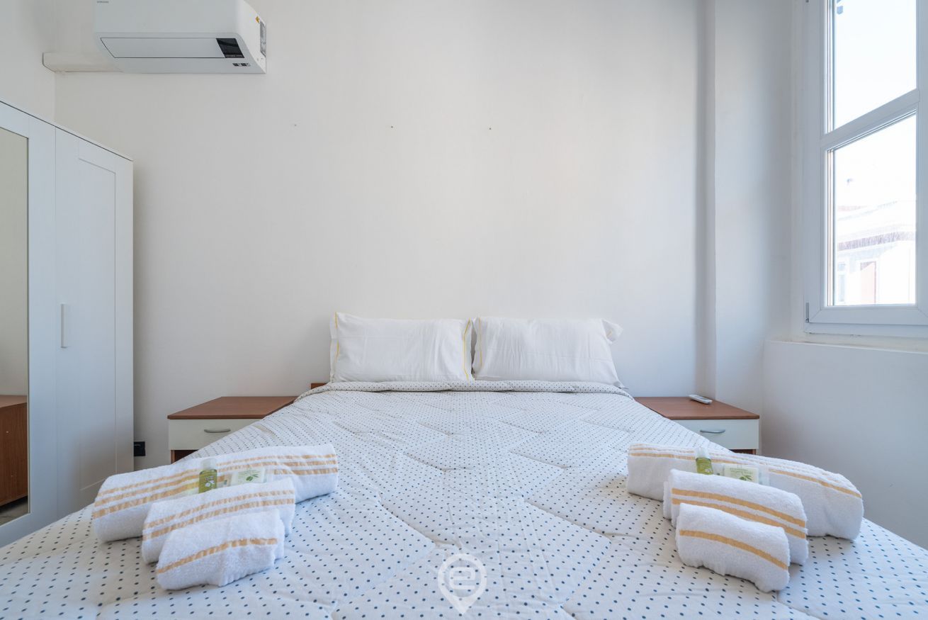 A bedroom with a bed, two nightstands, a wardrobe, and an air conditioning unit.