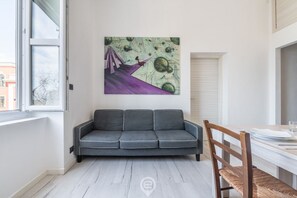 Un salon moderne avec un canapé gris, une table à manger en bois et des chaises, ainsi qu’un grand tableau abstrait accroché au mur.