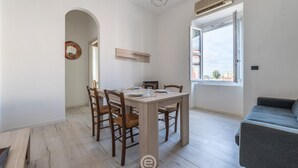 Un espace repas comprenant une table et des chaises en bois, un luminaire suspendu et une fenêtre donnant sur des immeubles.