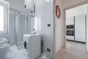 Une salle de bain moderne dotée d’une douche à parois de verre, d’un lave-linge encastré et d’un espace cuisine ouvert avec un four à micro-ondes et un four traditionnel.