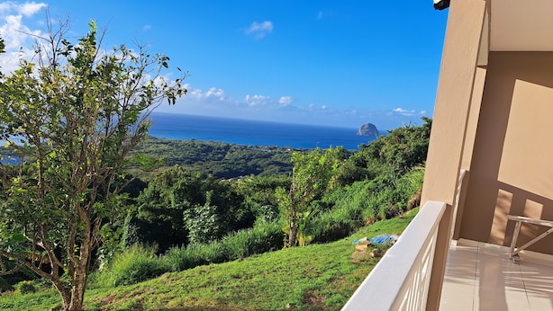 A balcony with a view of a lush green landscape and the ocean. - Villa LE Rocher (Le Diamant)