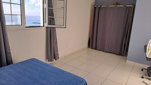 A room with a bed, a window with curtains, a shower area, and a fan. - Villa LE Rocher (Le Diamant)