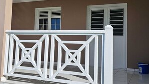 A building facade with two windows, a white decorative fence, and a blue bucket on the ground. - Villa LE Rocher (Le Diamant)