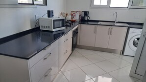 A modern kitchen with a microwave, toaster, and coffee maker on the counter, a washing machine, and a sink. - Villa LE Rocher (Le Diamant)