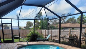 Une piscine couverte avec une terrasse en briques, une chaise longue et une clôture en bois en arrière-plan.