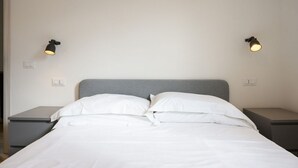 Una cama con sábanas blancas, dos mesitas de noche y dos lámparas de pared.