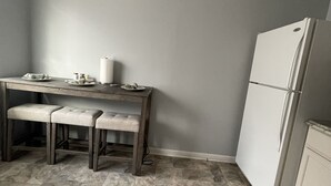 Eine Küche mit Holztisch, zwei Hocker, einem Kühlschrank und einem gefliesten Boden.