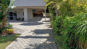 A house with a paved driveway leading to a covered entrance. - Iconic Wainui Beach a 100m stroll. Relax in Tropical type surroundings. (Gisborne)