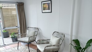 A room with two wicker chairs, a patterned rug, a potted plant, and a framed picture on the wall. - Iconic Wainui Beach a 100m stroll. Relax in Tropical type surroundings. (Gisborne)
