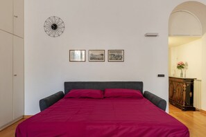 Un dormitorio con una cama, un armario, un reloj de pared y tres cuadros enmarcados.