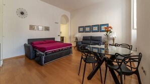 Ein gemütlicher Raum mit Bett, Sofa, Esstisch mit Stühlen und einer kleinen Küchenzeile.