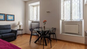 Ein Zimmer mit Esstisch, Stühlen, einer Couch, einer Lampe und einem Heizkörper.