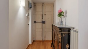 Ein Flur mit geschlossener Tür, einer Wandleuchte, einer Dekokabine mit Blumenvase und einem Heizkörper.