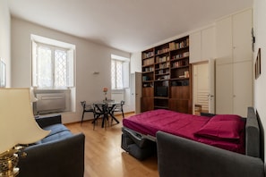 Una habitación pequeña con una cama, un escritorio, una silla, una estantería y un radiador.