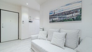 Una habitación de hotel moderna con un sofá blanco, un cuadro de un paisaje urbano en la pared y una puerta a la izquierda.